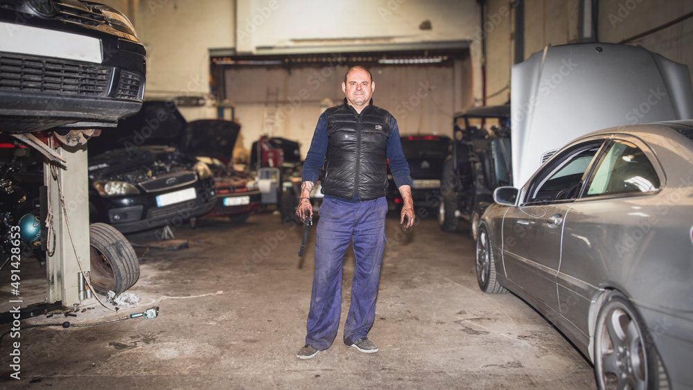 Portrait of mechanic in workshop surrounded by cars looking at camera