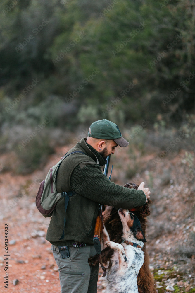 Hunter with his shotgun petting his two dogs in mountains