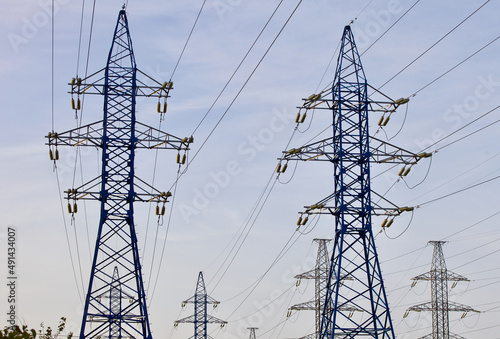 High voltage power lines pylons and electrical cables on a clear blue sky background. Modern infrastructure of high voltage transmission lines. Overhead power lines towers equipment. Energy industry.