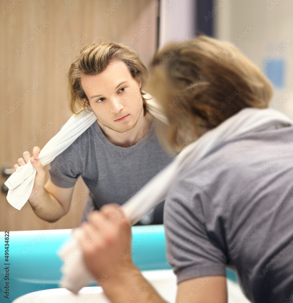 Obraz premium young man looking in the mirror,combing his hair,looking at problems on face.