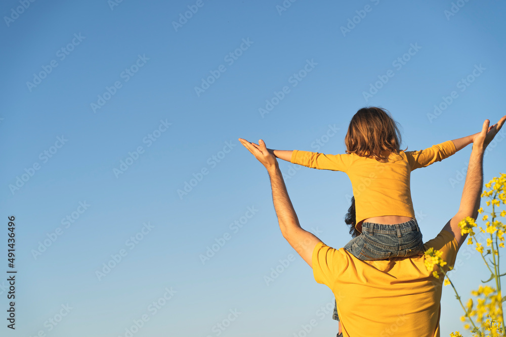 Dad holds his daughter on his shoulders. Portrait of a young father carrying his daughter on his back. father's day. Dad and son playing together outdoors on a summer. Family happiness love concept Dad holds his daughter on his shoulders. Portrait of a young father carrying his daughter on his back. father's day. Dad and son playing together outdoors on a summer. Family happiness love concept