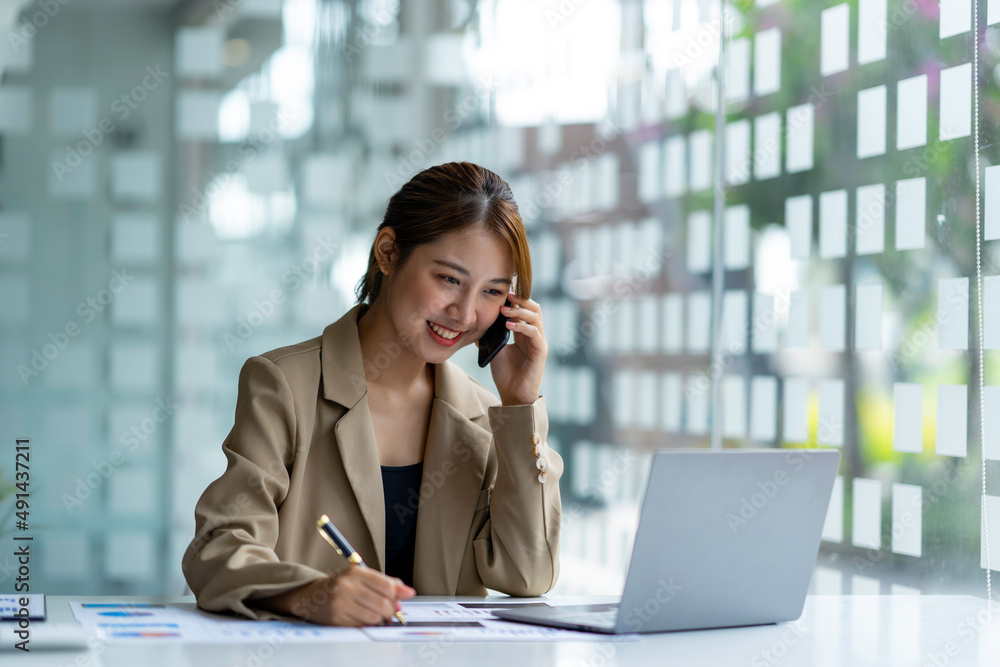 Fototapeta premium Portrait of a business woman using a laptop and talking on the phone with a customer. Happy working in the office
