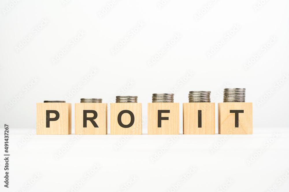 profit text written on wooden block with stacked coins on white background profit text written on wooden block with stacked coins on white background