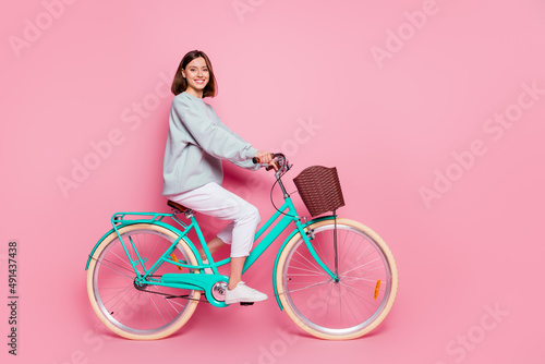Full length profile side photo of youth cheerful girl enjoy trip on bicycle isolated over pink color background photo