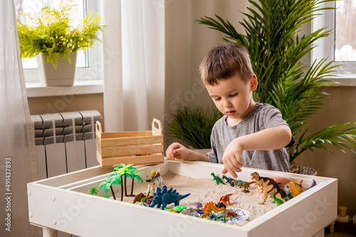 Fototapeta Cute baby boy playing sensory box kinetic sand table with carnivorous and herbiv