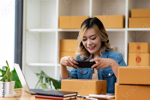 Small business entrepreneur SME, asian young woman owner packing product, checking parcel box delivery, using smartphone receive order from customer, working at home office. Merchant online, ecommerce