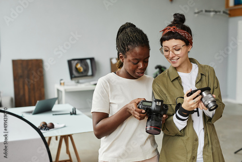 Obraz na plátne Waist up portrait of two female photographers holding cameras while working in p