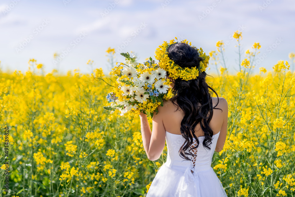 Portrait of a beautiful woman with a wreath of yellow flowers on her head. A girl with a bouquet in a rapeseed field. Photo from the back Portrait of a beautiful woman with a wreath of yellow flowers on her head. A girl with a bouquet in a rapeseed field. Photo from the back