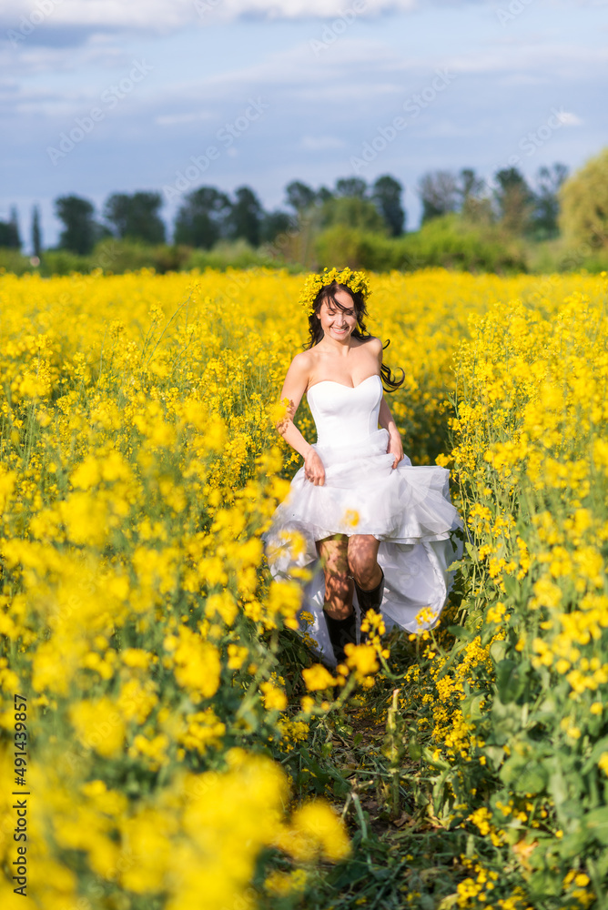 young beautiful woman runs through a field with yellow flowers. The bride in a long white dress and boots in a rapeseed field. young beautiful woman runs through a field with yellow flowers. The bride in a long white dress and boots in a rapeseed field.