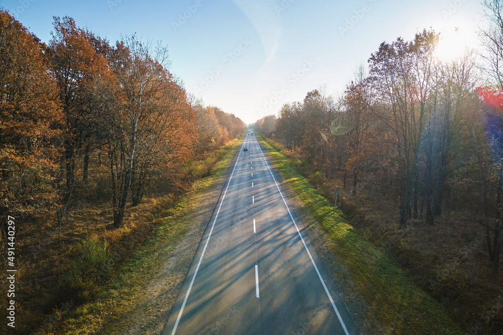 Aerial view of empty intercity road between autumn woods at sunset. Top view from drone of highway in evening