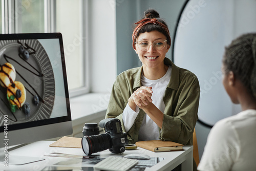 Portrait of smiling female photographer collaborating with colleague or client while discussing images in studio photo