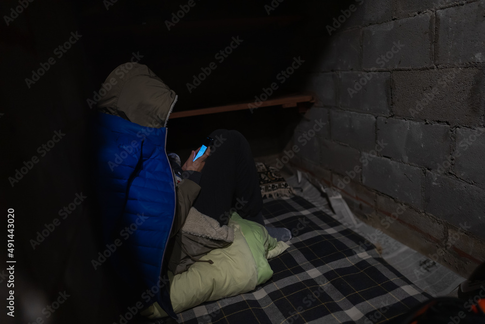 Woman in jacket is sitting and reading war news in a basement during russian invasion Woman in jacket is sitting and reading war news in a basement during russian invasion