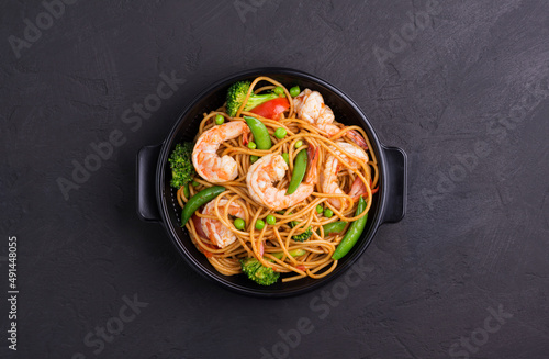 Stir-fried spaghetti or stir-fry noodles with vegetables and shrimp in a black bowl. dark background, top view, copy space