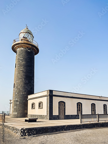 Big tall stone lighthouse on a blue sky background. No people. Nature wallpaper.