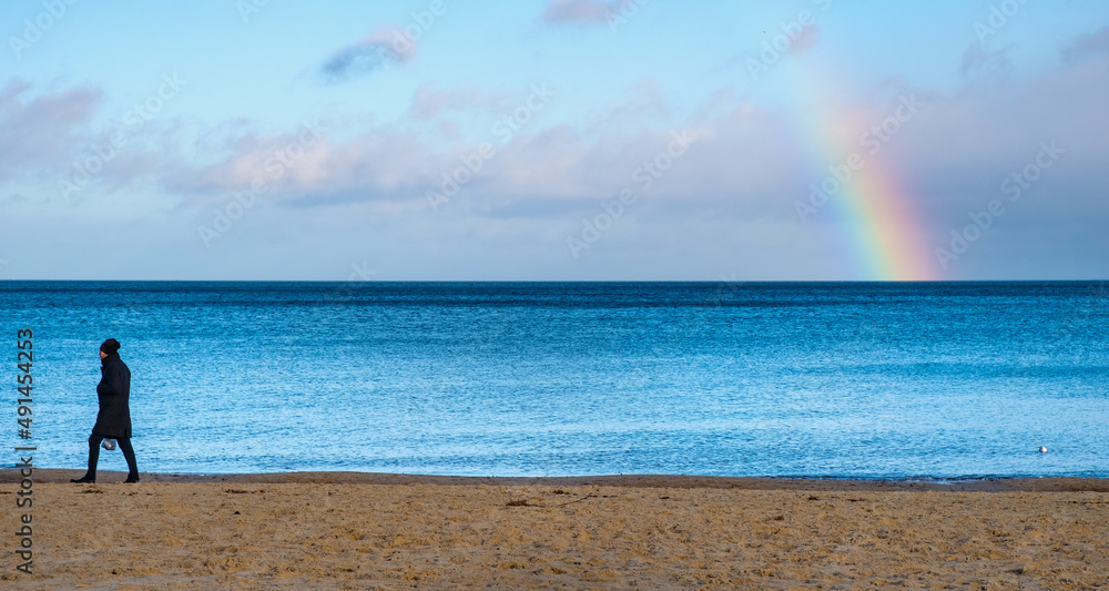 Panoramic winter view of Baltic sea with lonely person walking along beach and rainbow over horizon offshore Gdynia Orlowo of Tricity in Pomerania region of Poland Panoramic winter view of Baltic sea with lonely person walking along beach and rainbow over horizon offshore Gdynia Orlowo of Tricity in Pomerania region of Poland
