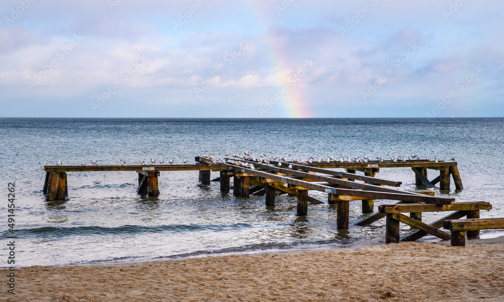 Winter rainbow seascape of Baltic sea with vintage jetty platform over beach of Gdynia Orlowo district of Tricity in Pomerania region of Poland