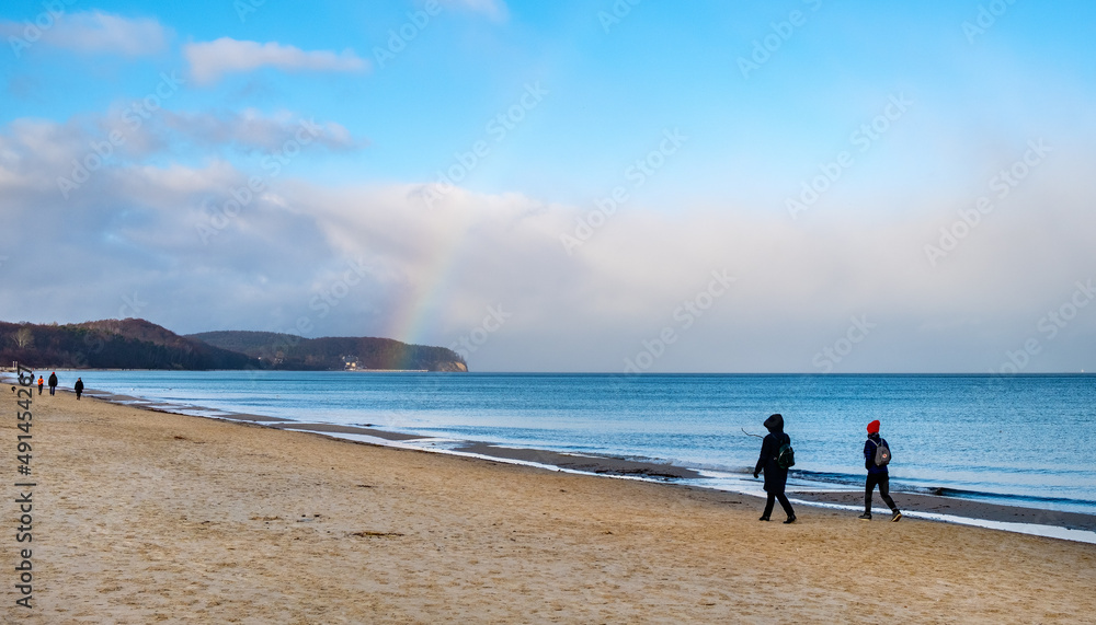 Panoramic winter view of Baltic sea with people walking along beach offshore Gdynia Orlowo of Tricity with rainbow in Pomerania region of Poland Panoramic winter view of Baltic sea with people walking along beach offshore Gdynia Orlowo of Tricity with rainbow in Pomerania region of Poland