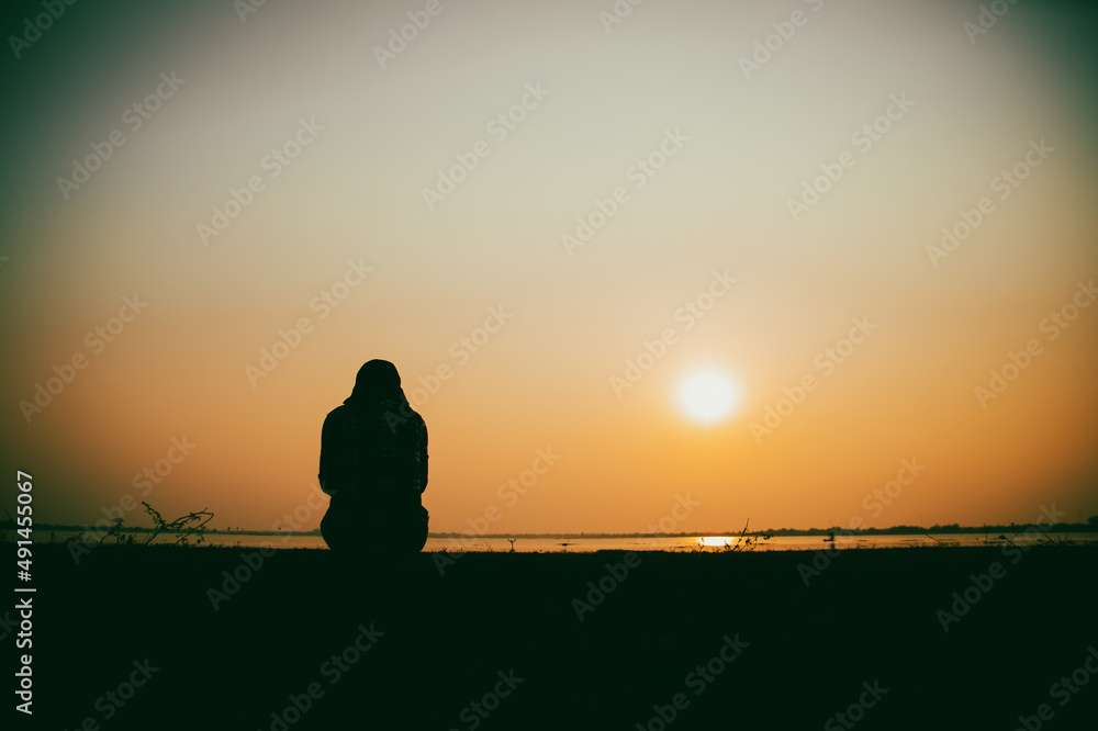 Silhouette of the woman sitting sad at the river during sunset