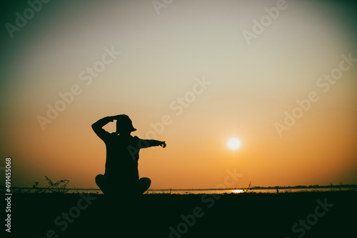 Silhouette of the woman sitting sad at the river during sunset