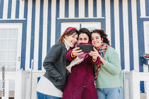 happy women friends using mobile phone in front of colorful houses.Costa Nova, Aveiro, Portugal
