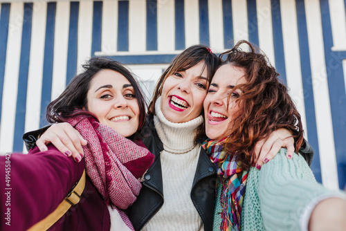 happy women friends using mobile phone in front of colorful houses.Costa Nova, Aveiro, Portugal