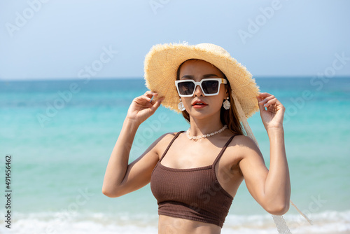 Beautiful woman wearing sunglasses at beach on sunny day, Asian woman in bikini and sun hat standing on sea beach. Summer vacation © Pituk