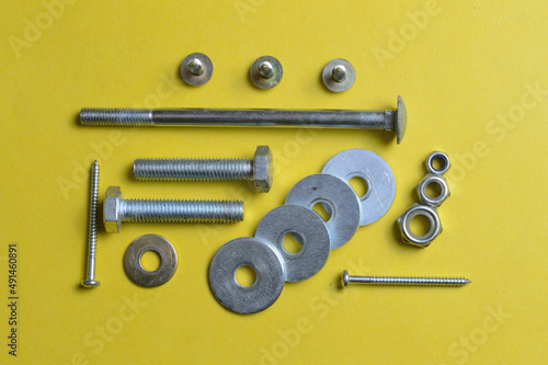 nut bolts and self-tapping screws of different sizes lie on a yellow background. close-up.