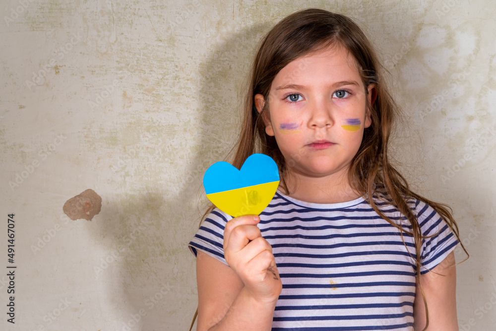 Stop war in Ukraine concept. Little Ukrainian blond girl, with the flag of ukraine in the heart in a ruined old house. Save the children, close the sky of Ukraine, humanitarian aid disaster concept