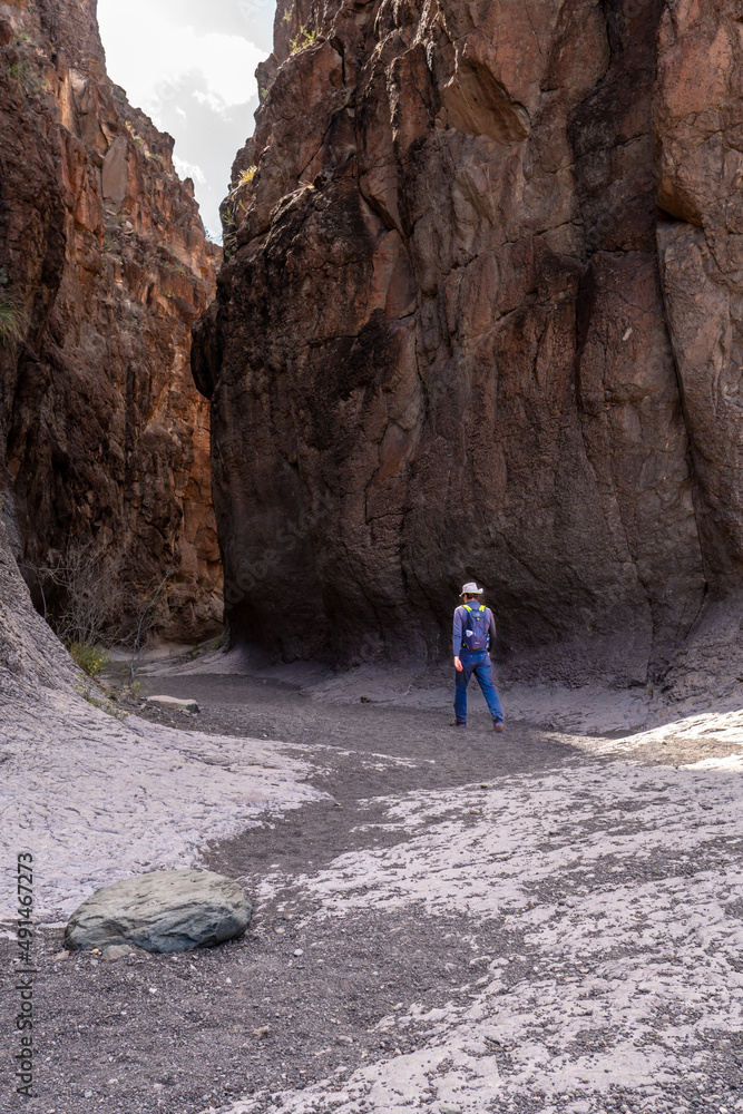Hiker man person Caucasian mature walking into a slot canyon in a gravel washed trail, Closed Canyon, Big Bend Ranch State Park, Texas