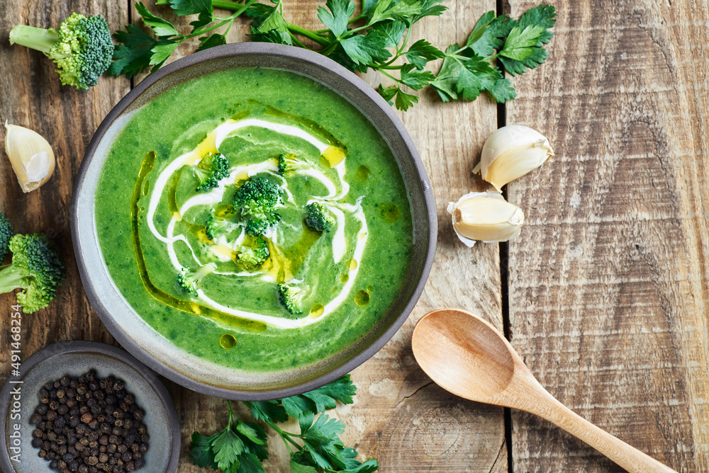 Fresh creamy broccoli soup on wooden table. Green healthy vegan broccoli soup served with cream and olive oil in bowl on wooden table. Fresh creamy broccoli soup on wooden table. Green healthy vegan broccoli soup served with cream and olive oil in bowl on wooden table.