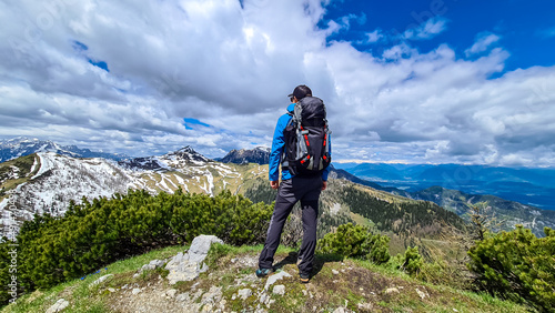 Hiker man with backpack at the summit of Hahnkogel (Klek) with scenic view on mountain peaks in the Karawanks and Julian Alps, Carinthia, Austria. Border with Slovenia. Triglav National Park © Chris