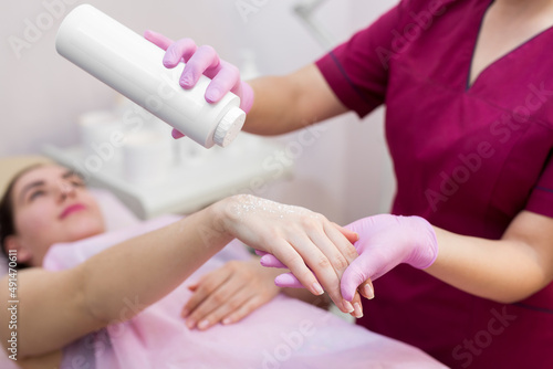 Close-up of a beautician sprinkles talcum powder on a young girl s hand before the depilation procedure. The girl lies on a couch in a beauty salon  she does the procedure shugaring