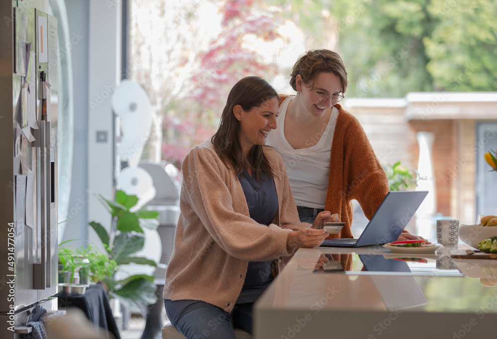 Happy women friends online shopping at laptop in kitchen Happy women friends online shopping at laptop in kitchen
