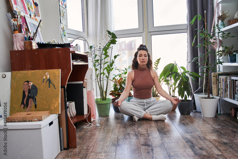 Mindful young woman sitting in lotus position at the floor at home Mindful young woman sitting in lotus position at the floor at home