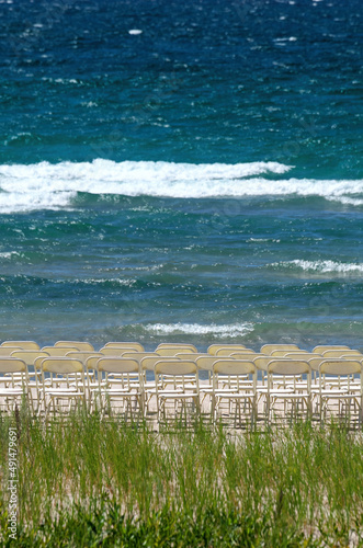 White Folding Chairs Arranged in Rows for a Wedding at a White Sandy Beach on a Sunny Summer Day photo