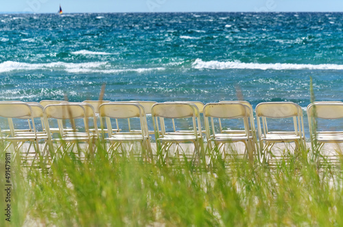 White Folding Chairs Arranged in Rows for a Wedding at a White Sandy Beach on a Sunny Summer Day