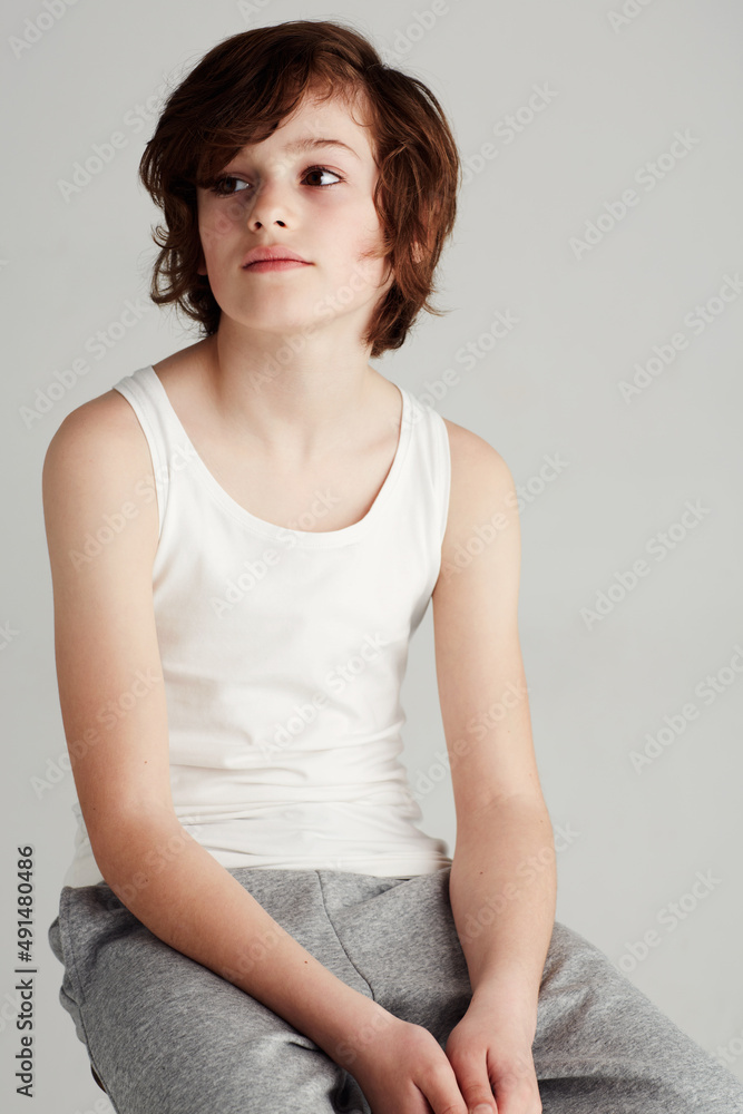 Candid and casual. A young boy sitting on a stool in the studio while looking away. Candid and casual. A young boy sitting on a stool in the studio while looking away.