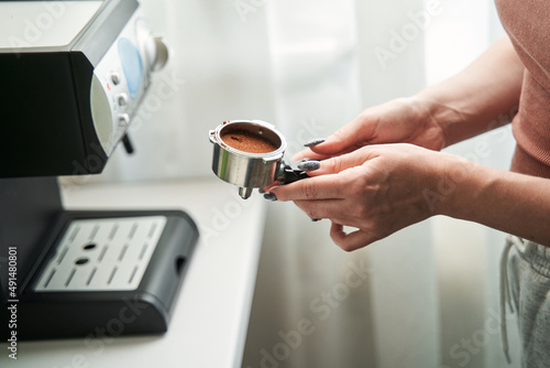 Woman holding device with ground coffee while preparing her morning drink at the kitchen