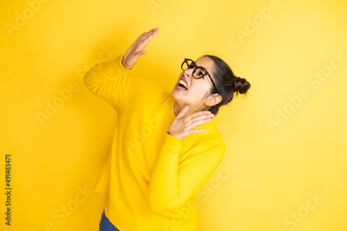 Young beautiful woman wearing casual sweater over isolated yellow background scared with her arms up like something falling from above
