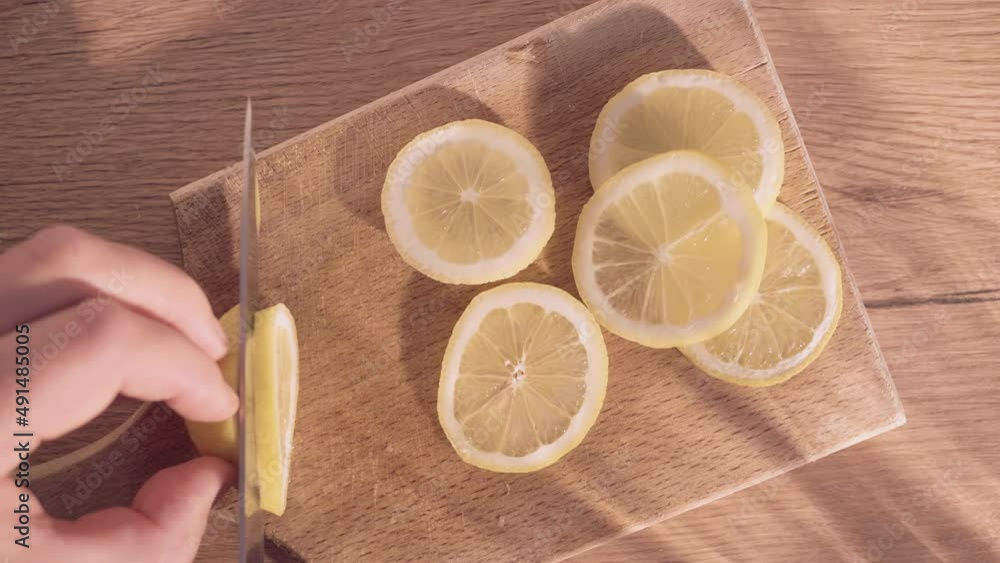 Close-up shot of Caucasian male hands cutting lemon on slices with a sharp knife on a wooden board. Male chef point of view shot. Close-up shot of Caucasian male hands cutting lemon on slices with a sharp knife on a wooden board. Male chef point of view shot.