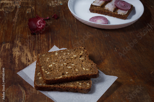 Ukrainian cuisine snack, sandwich with Borodino rye bread and prickled pork lard, red onions on white plate, wooden background. photo