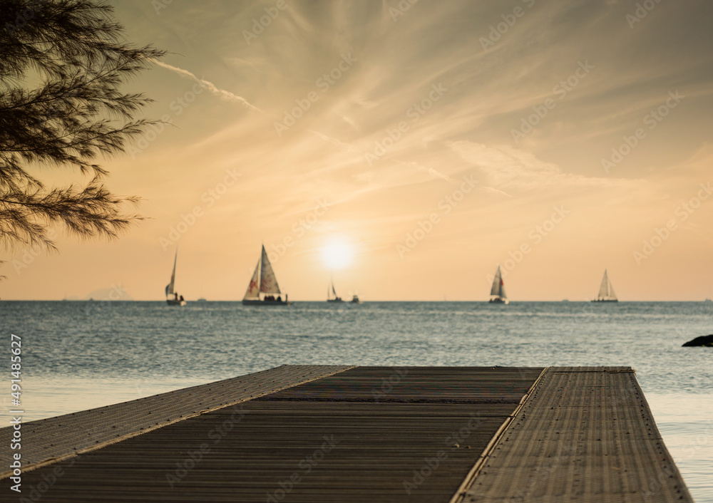 Obraz premium Wooden pier at sunset with sailboats in the background. selective focus