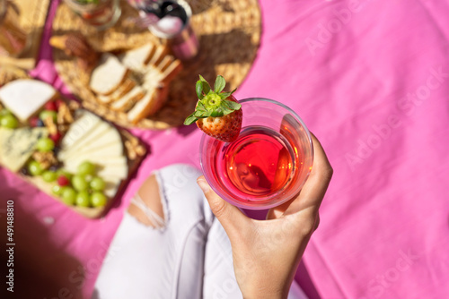Horizontal top view of unrecognizable woman drinking a strawberry juice outdoors. Above shot of woman holding a strawberry fruit juice on pink picnic background. Health and drink concept.