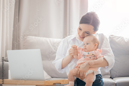 Woman freelancer working or online consultation with doctor from home office with baby on laptop internet work  sun light