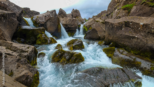 Beautiful landscape with a waterfall on a small mountain river in Iceland.  Clear Water flows in a stormy stream among stones and rocks covered with moss
