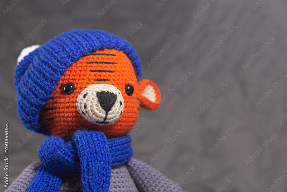 Soft knitted toy tiger portrait in a blue hat on a gray background Soft knitted toy tiger portrait in a blue hat on a gray background
