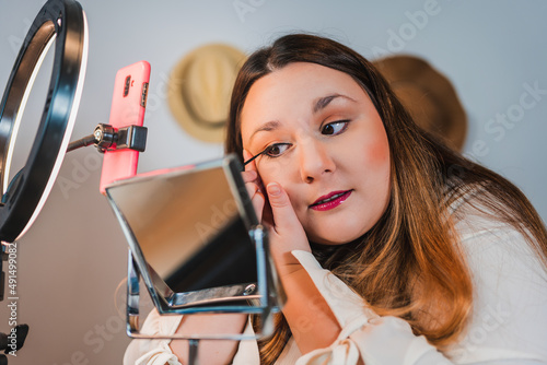 closeup of a plus size woman painting her eye making a video blog about cosmetics with her mobile