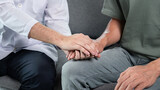 Man doctor holding hands with patient to giving encouraging while he receive to listening about result