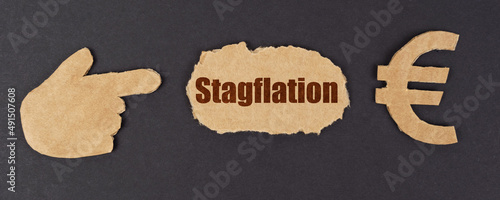 On a black surface, a figure of a hand, a euro symbol and a torn cardboard with the inscription - stagflation photo