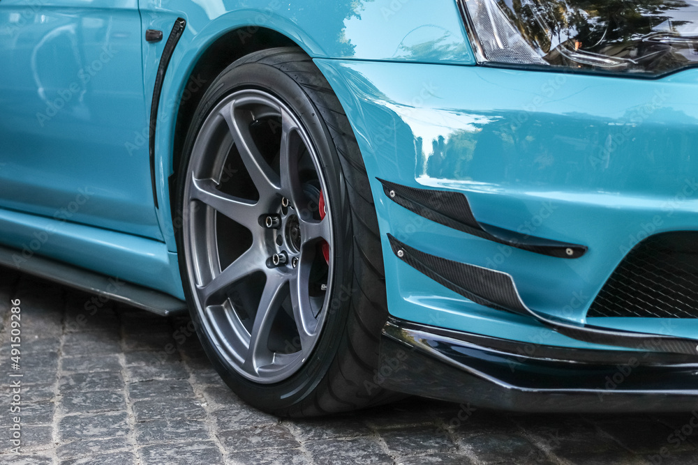 Close up of a wheel of a sports car. Gray car rim with low profile rubber. Blue sports car.